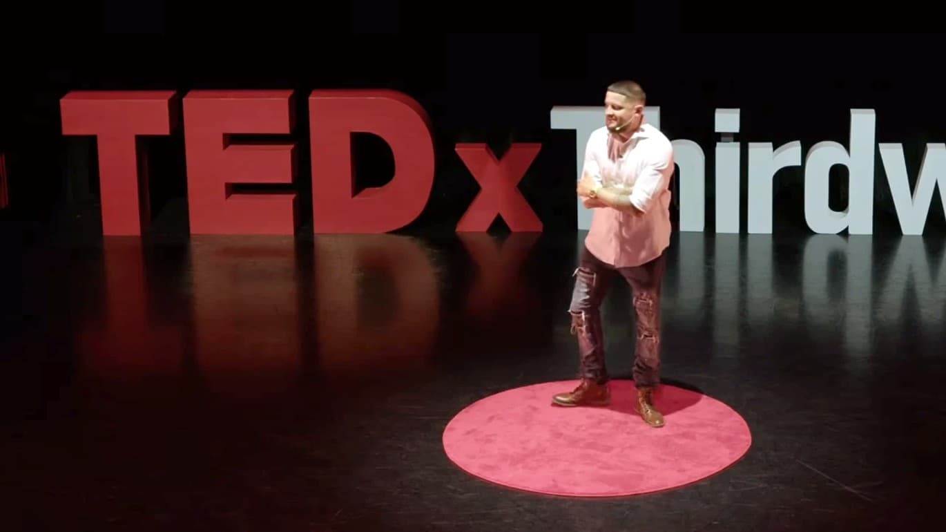 David Settle smiling on the red circle during his TEDxThirdWard talk, with the freestanding TEDx letters behind him